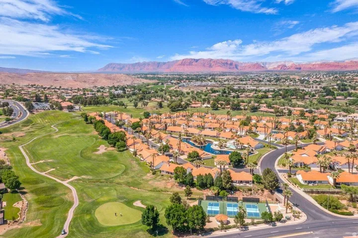 Expansive golf course, tennis courts, and swimming pool within a residential community featuring palm trees and red rock scenery