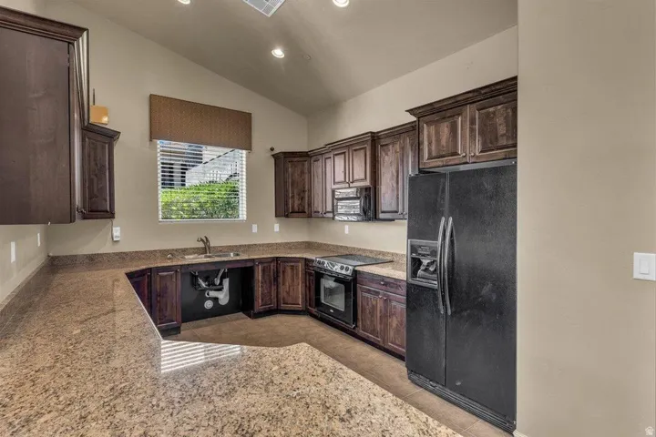 Kitchen featuring U-shaped stone-finish countertops, dark wood cabinetry, and a black appliance suite