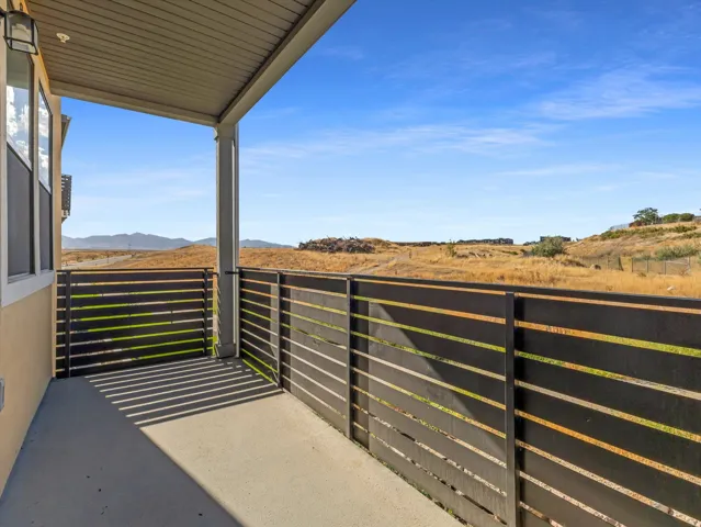 Covered outdoor patio with concrete flooring, modern slatted fencing, and exterior wall lighting