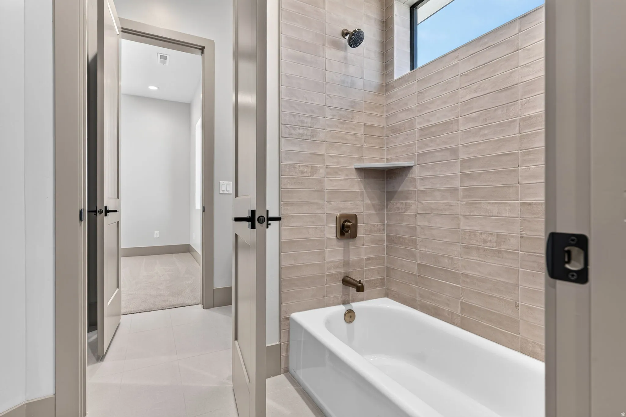 White soaking tub with floor-to-ceiling tile surround, bronze-finish fixtures, and integrated storage shelf