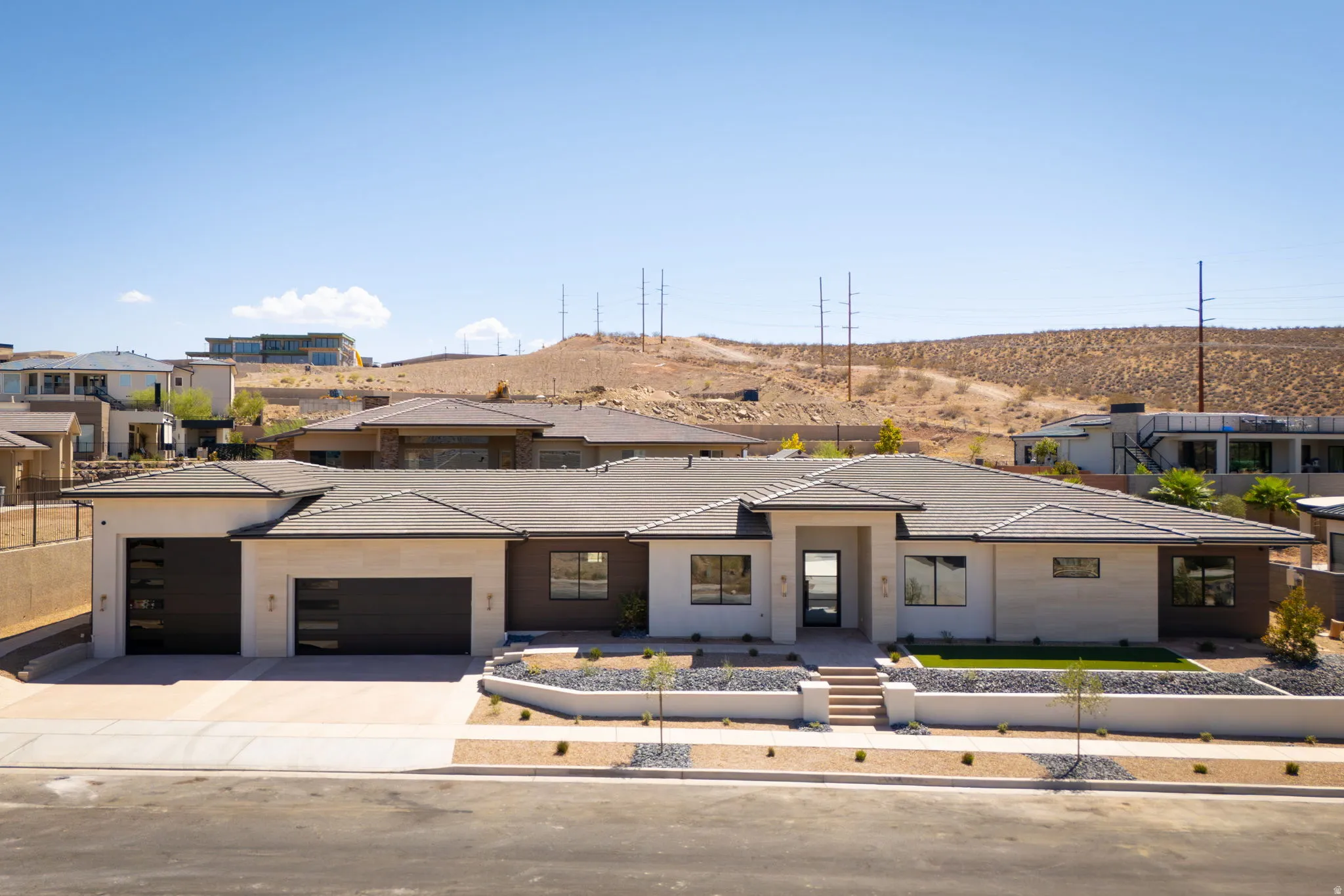 Modern desert architecture featuring a light-toned exterior, dark-framed windows, an integrated two-car garage, and a landscaped front yard with a low maintenance design