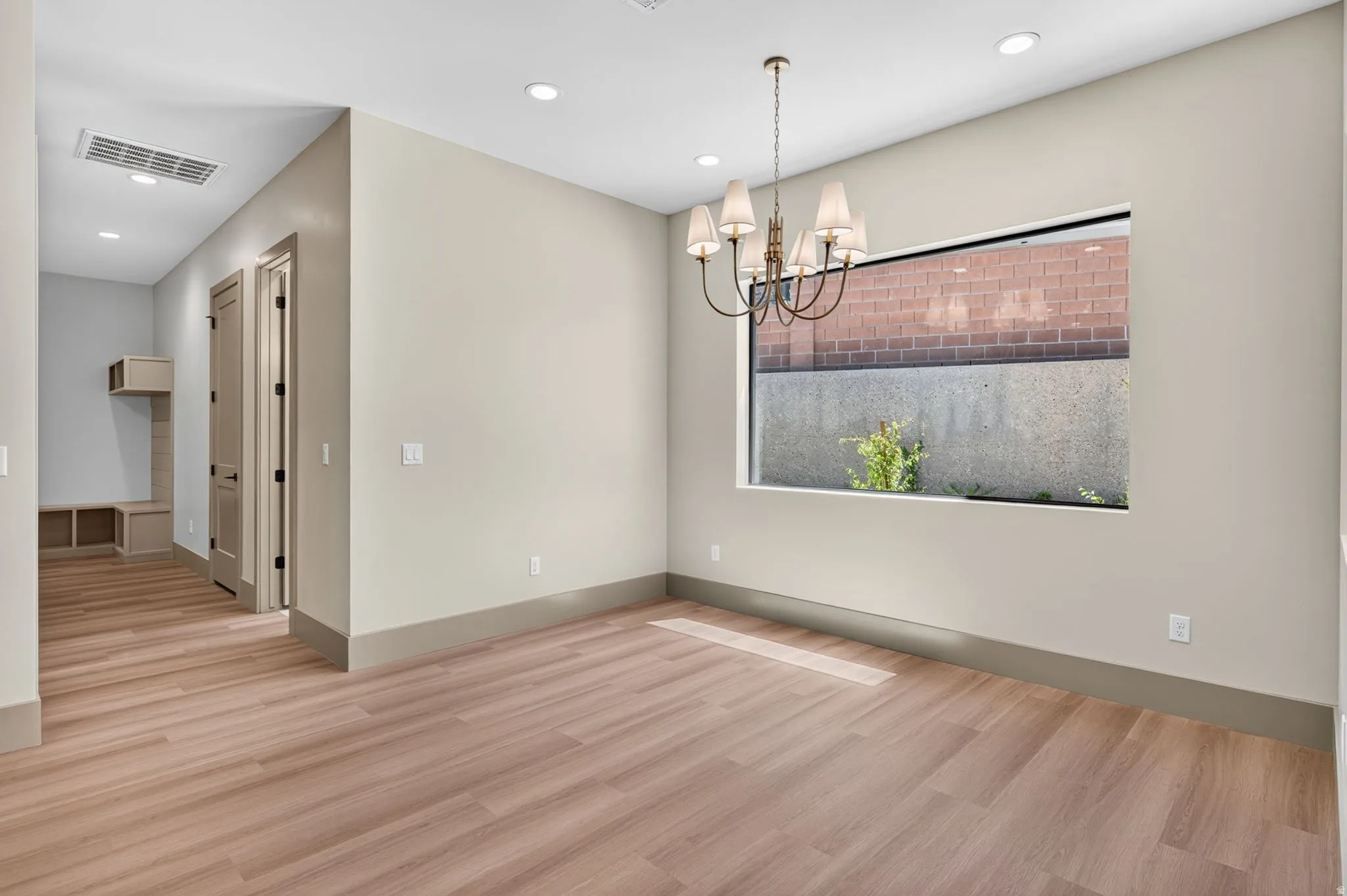 Wood-finish flooring throughout, recessed ceiling lighting, brass chandelier with sconces, horizontal window, and built-in entry shelving