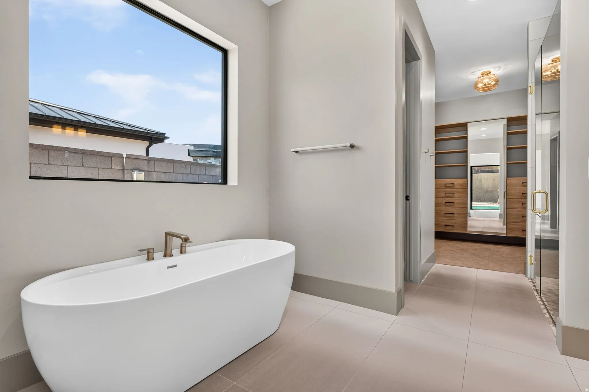 Freestanding soaking tub with brushed nickel fixtures, large picture window, and direct access to a custom built-in closet with integrated shelving