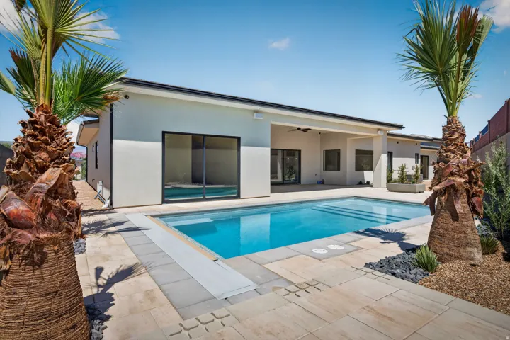 Rear exterior featuring a rectangular pool, concrete paver decking, and mature palm trees