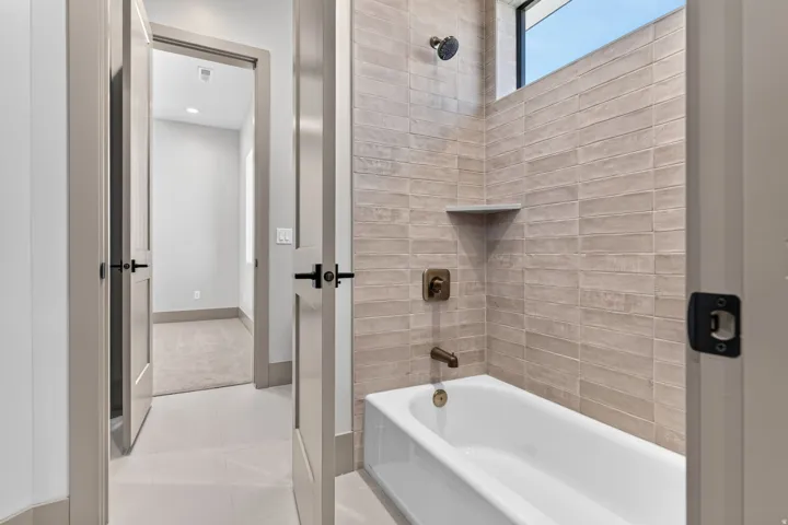 White soaking tub with floor-to-ceiling tile surround, bronze-finish fixtures, and integrated storage shelf