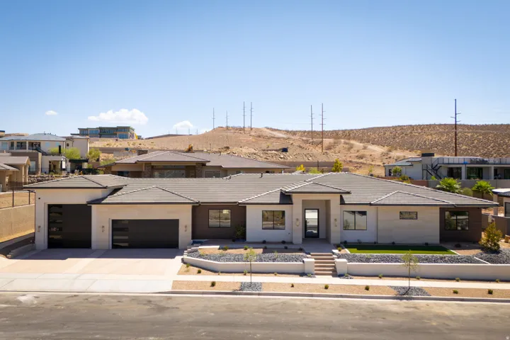 Modern desert architecture featuring a light-toned exterior, dark-framed windows, an integrated two-car garage, and a landscaped front yard with a low maintenance design