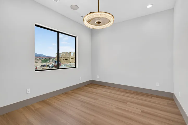 Spacious room featuring wood-finish flooring, a large window, a modern ceiling light fixture, recessed ceiling lighting, and integrated ceiling speakers