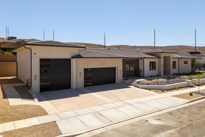 Contemporary exterior with stucco and stone accents, featuring a multi-car garage with modern doors, a paved driveway, and tiered xeriscaping