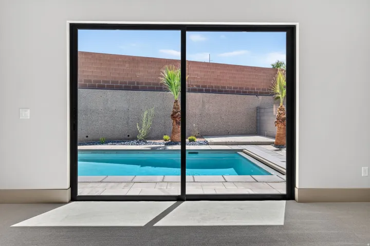 Expansive sliding glass doors opening to a private pool with tiled coping, surrounded by a low-maintenance hardscaped yard and mature palm trees