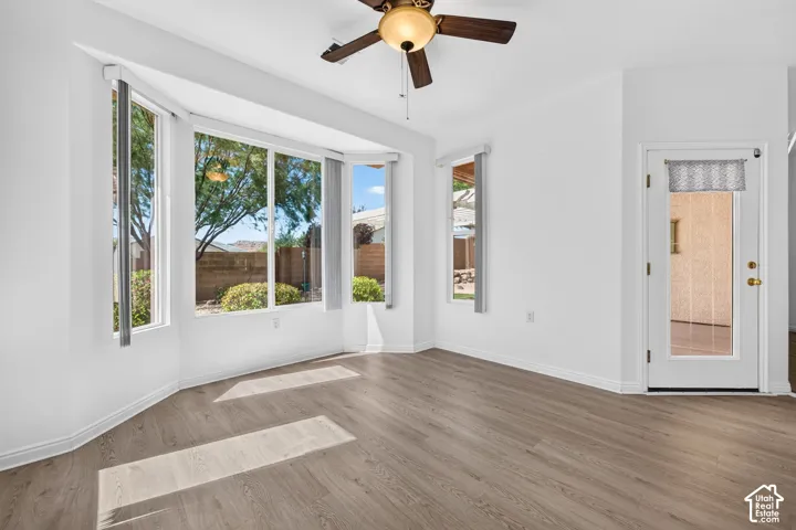 Bay window offering abundant natural light, wood-finish flooring, white walls, and a ceiling fan with light fixture