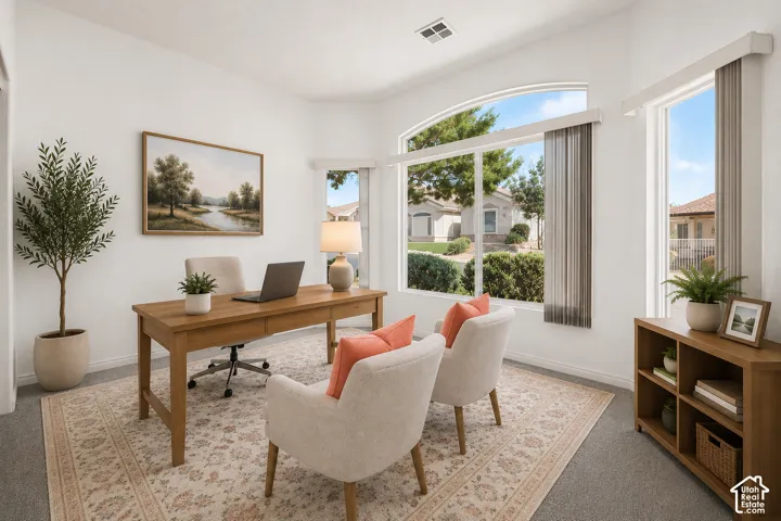 Bright home office featuring abundant natural light from oversized glass doors and windows, wood-finish desk with integrated workspace, neutral upholstered seating, geometric area rug, wood-frame wall art, and built-in shelving with open storage cubbies