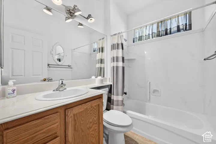 Bright bathroom featuring a wood-finish vanity with a white countertop and round ceramic sink, white subway tile walls, an integrated bathtub-shower combination with striped curtain, a white toilet, and recessed ceiling lighting