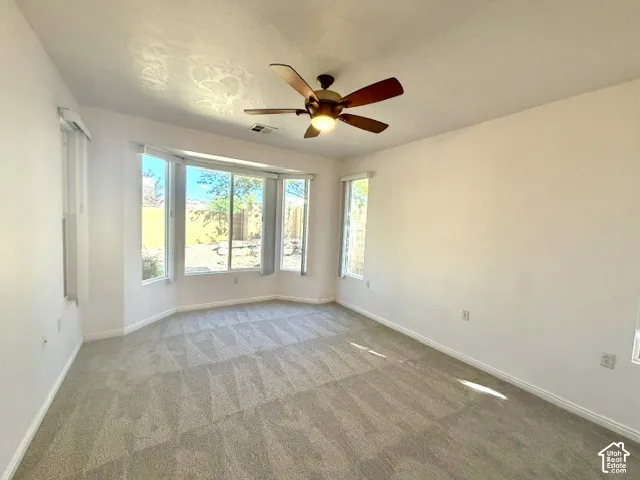 Bay window with multiple panels, ceiling fan with integrated lighting, and neutral carpeting