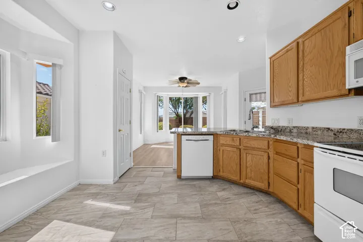 Bright, open kitchen featuring wood-finish cabinetry, granite countertops, white appliances, and herringbone-pattern tile flooring