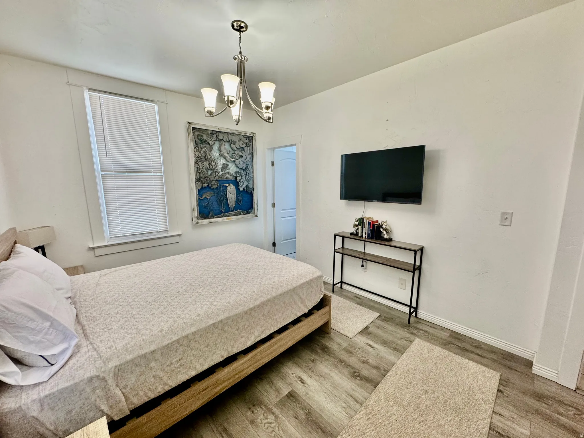 Room featuring wood-finish flooring, a contemporary chandelier, and a window with blinds