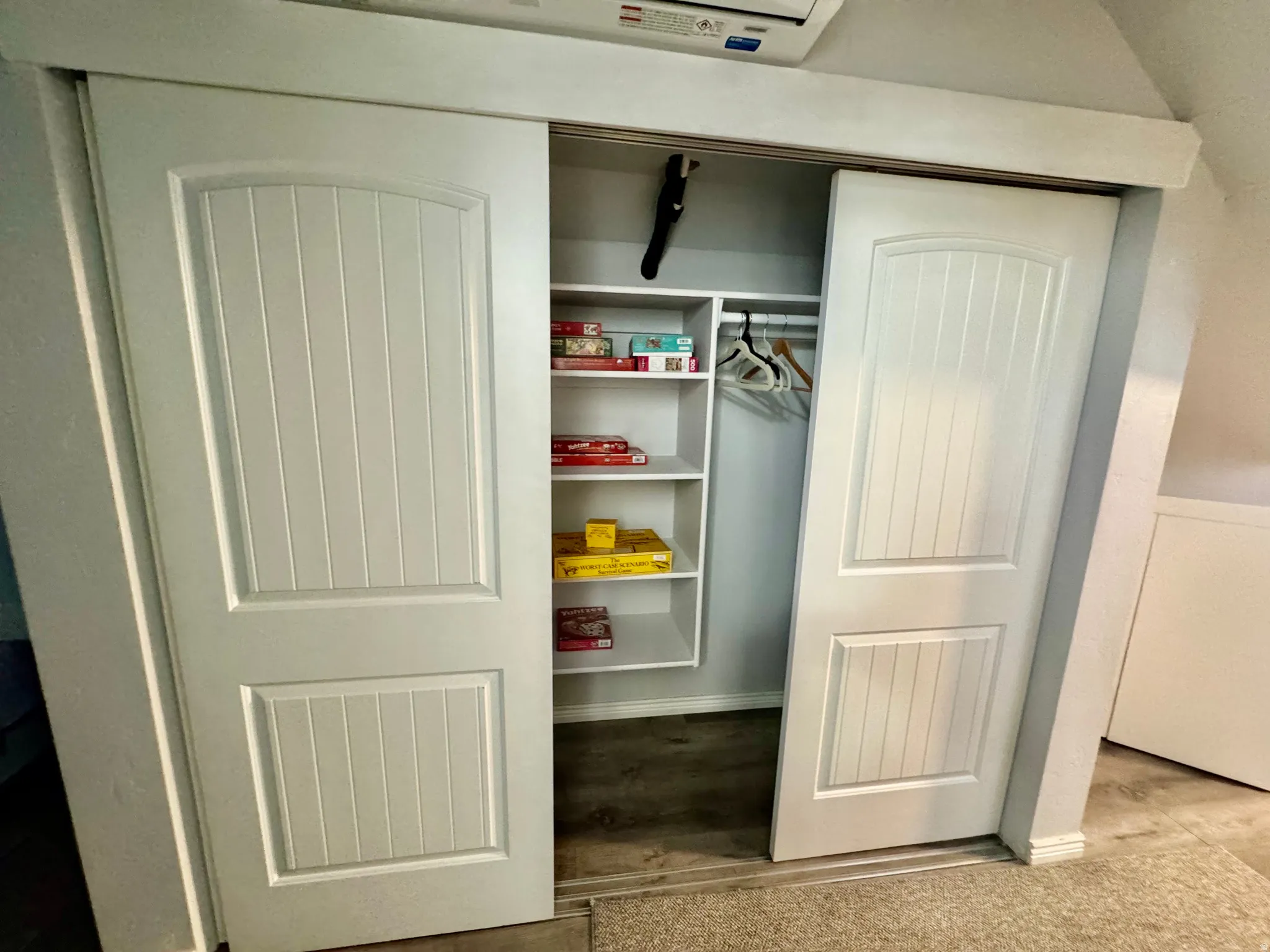 White sliding barn doors with vertical paneling, featuring a built-in closet system with open shelving and a clothing rod