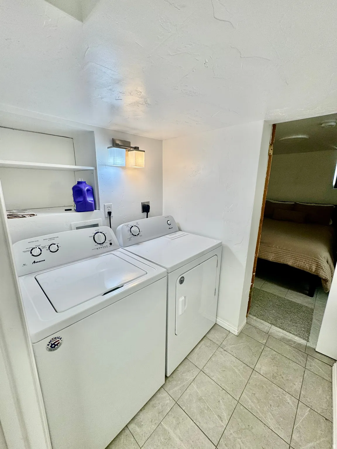 Dedicated laundry area featuring a top-load washing machine and front-load dryer, integrated wall shelving, and overhead lighting