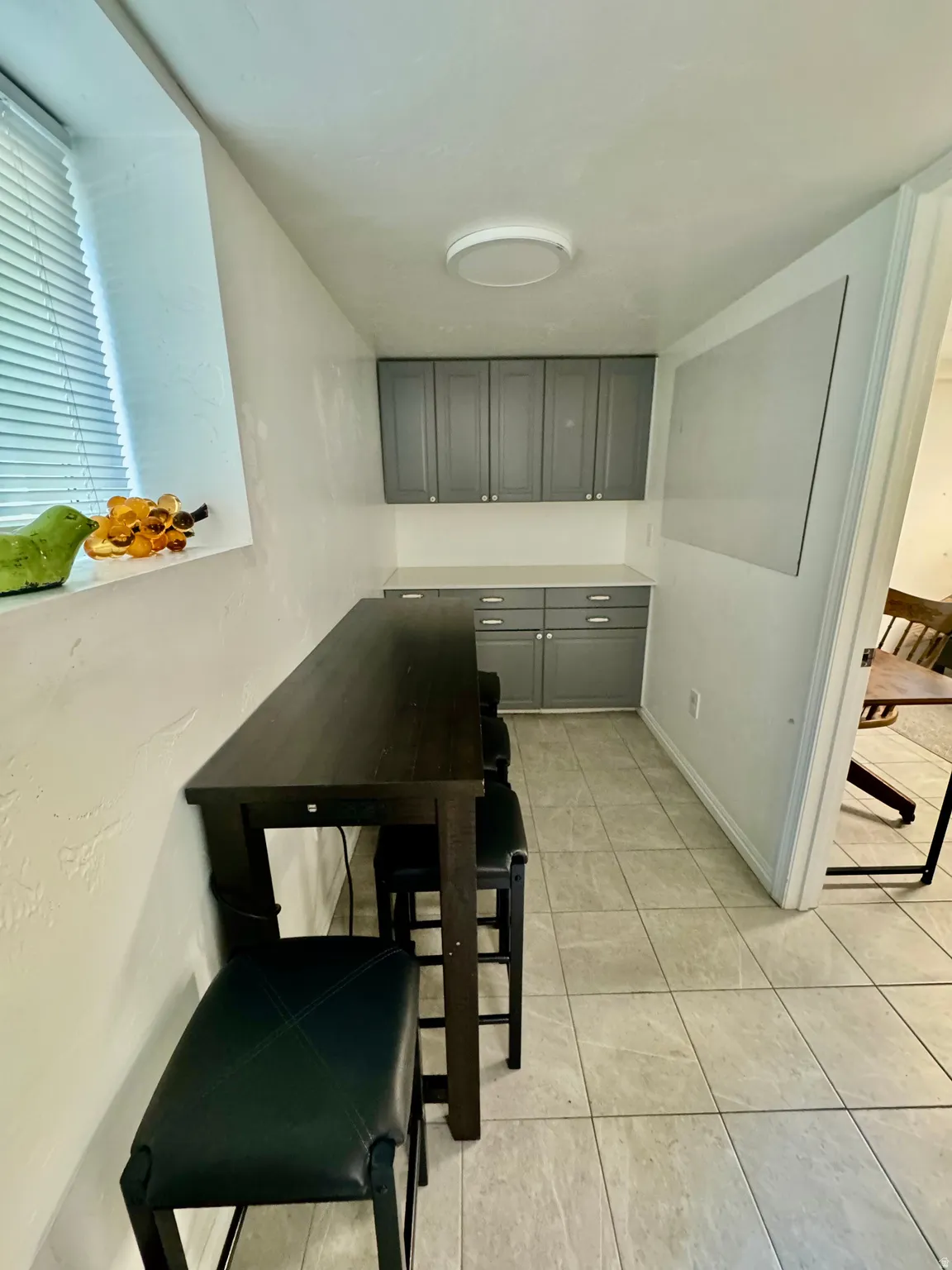 Compact kitchen area featuring grey shaker-style cabinetry, a light-toned countertop, and tiled flooring