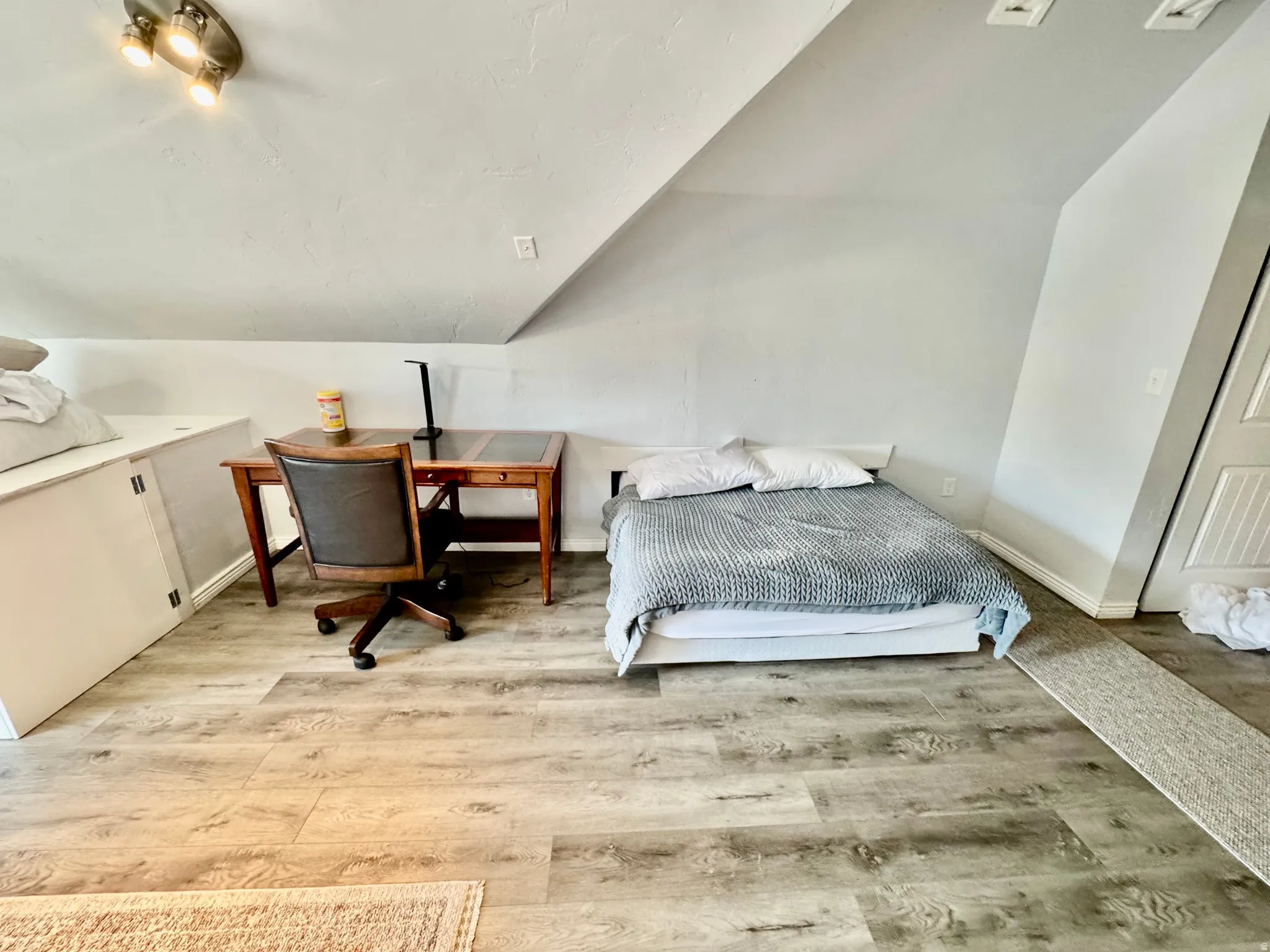 Versatile loft space featuring sloped ceilings, recessed wall panels, and wood-finish flooring