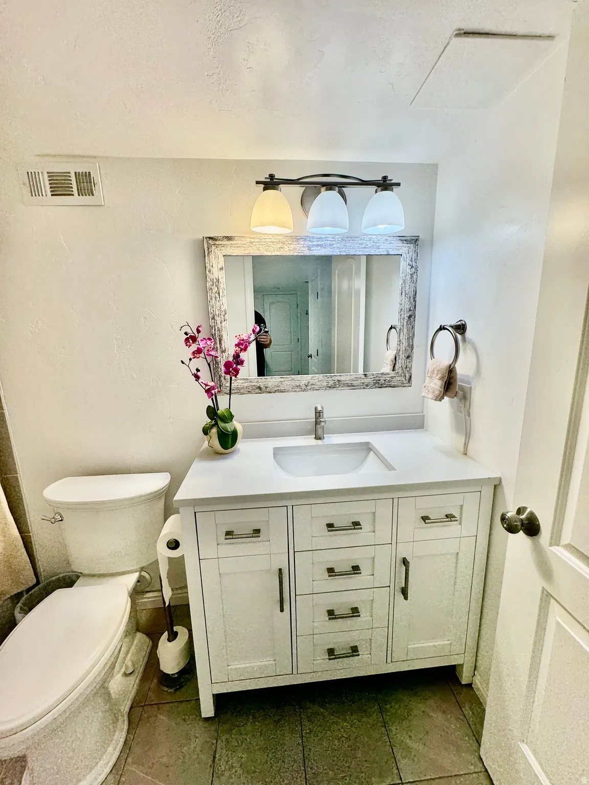 White shaker vanity with a single basin, complemented by a distressed wood-frame mirror and a three-light fixture