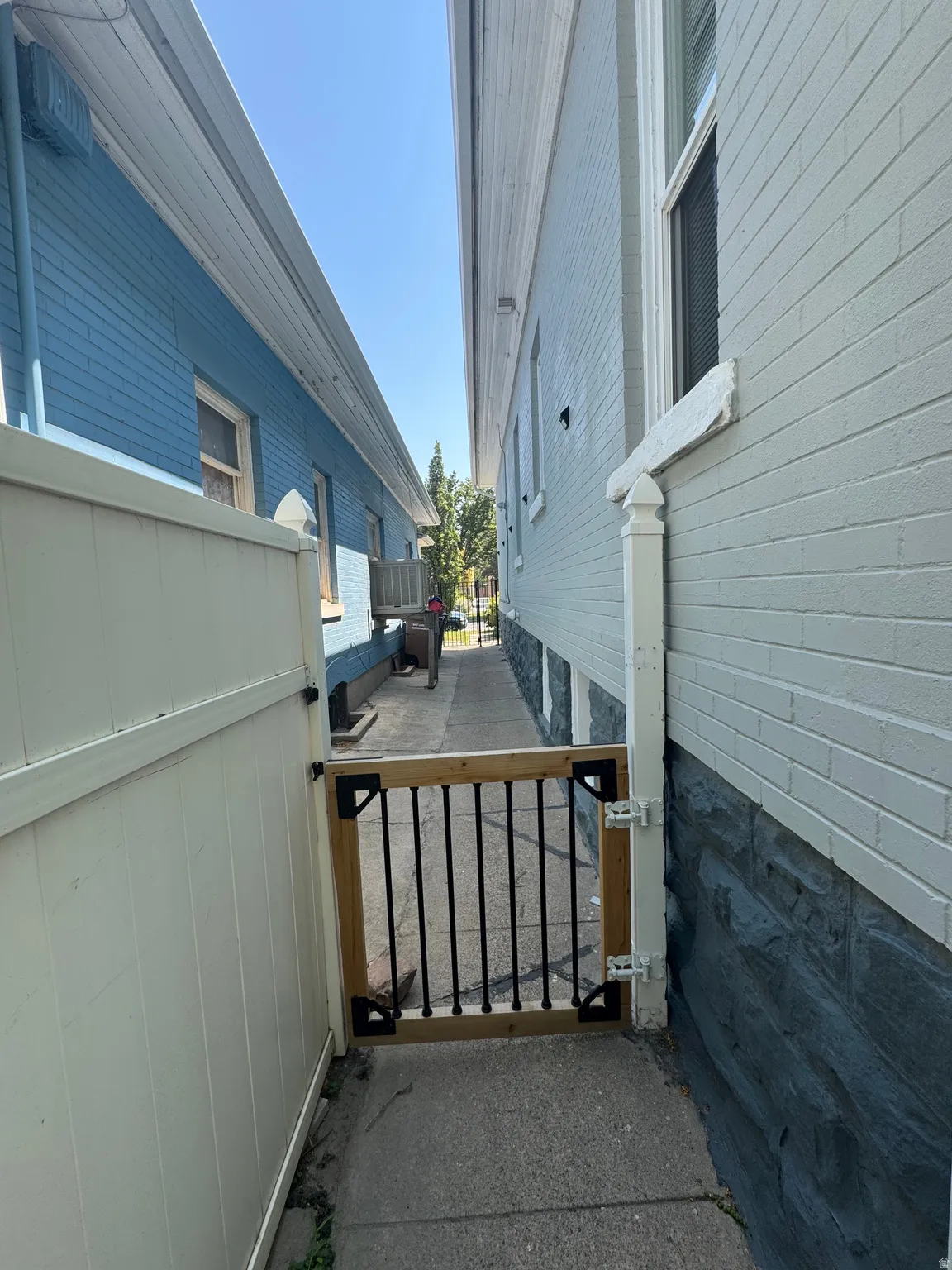 Side property access featuring a wood and wrought iron gate, concrete walkway, and vinyl fencing