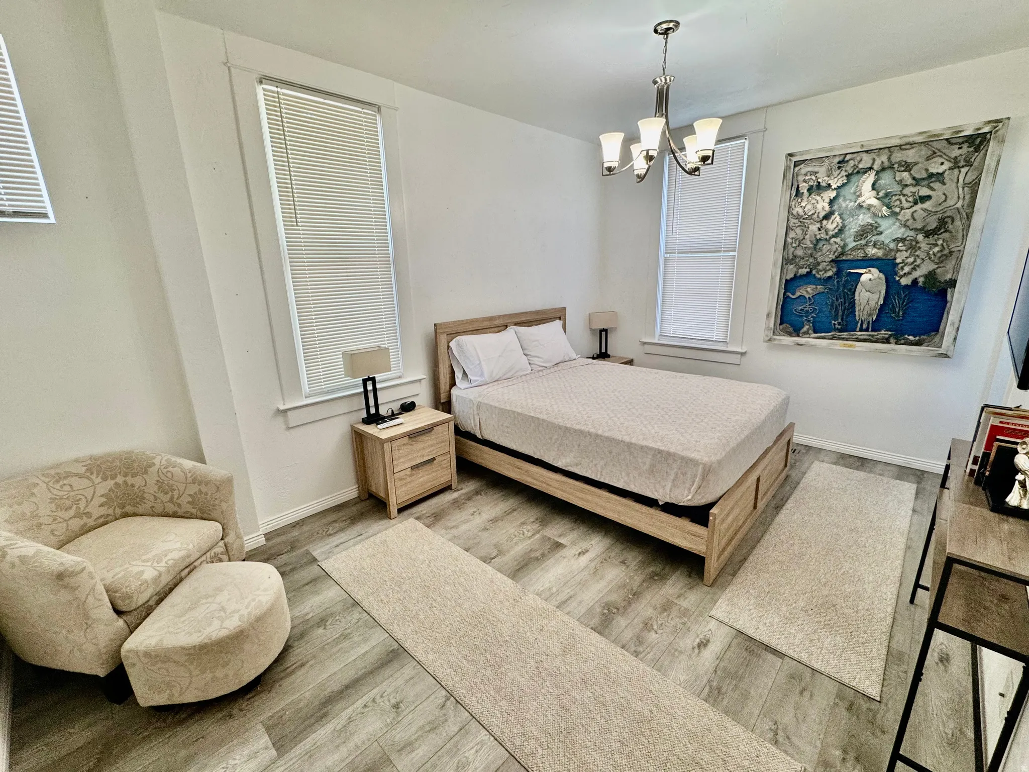 Bright room featuring two windows with blinds, wood-finish flooring, and a multi-bulb chandelier