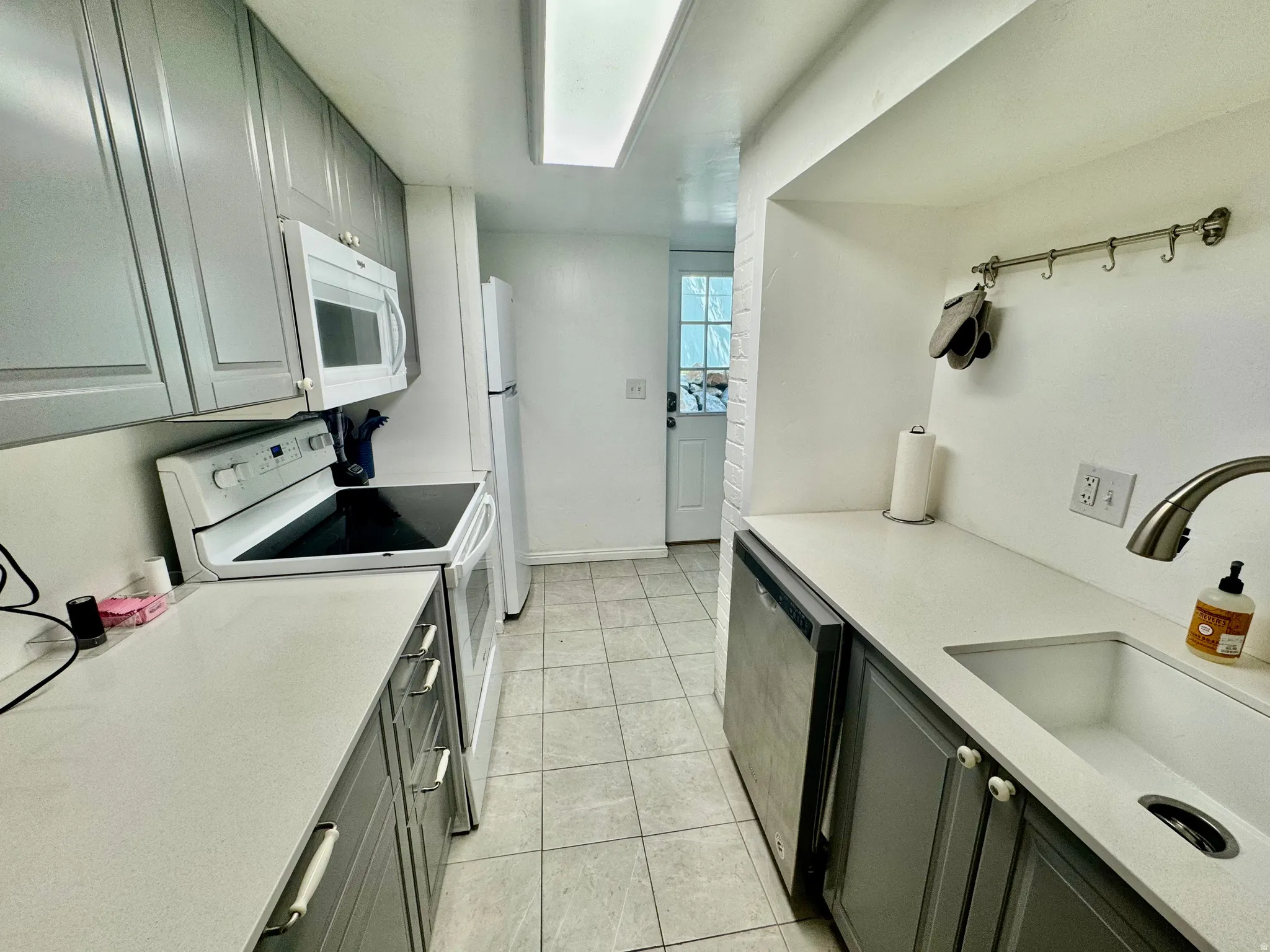 Kitchen featuring light gray cabinetry, white countertops, stainless steel sink with gooseneck faucet, white appliances, and tiled flooring