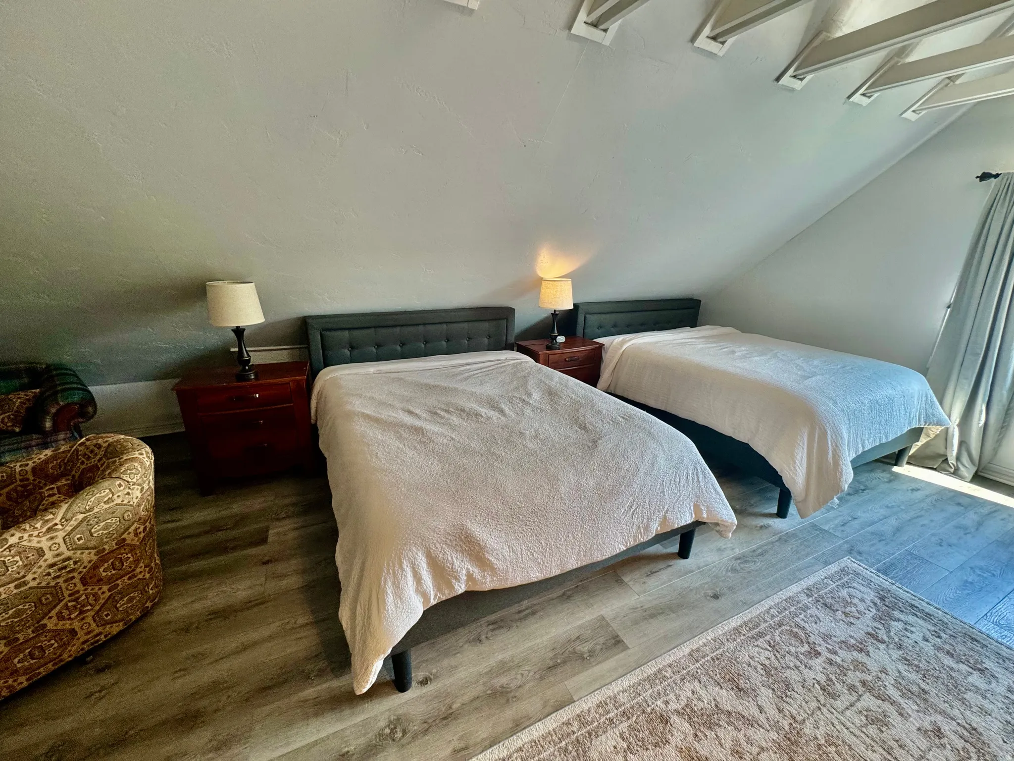 Room featuring sloped ceilings with exposed white rafters, wood-finish flooring, and light-filtering window treatments