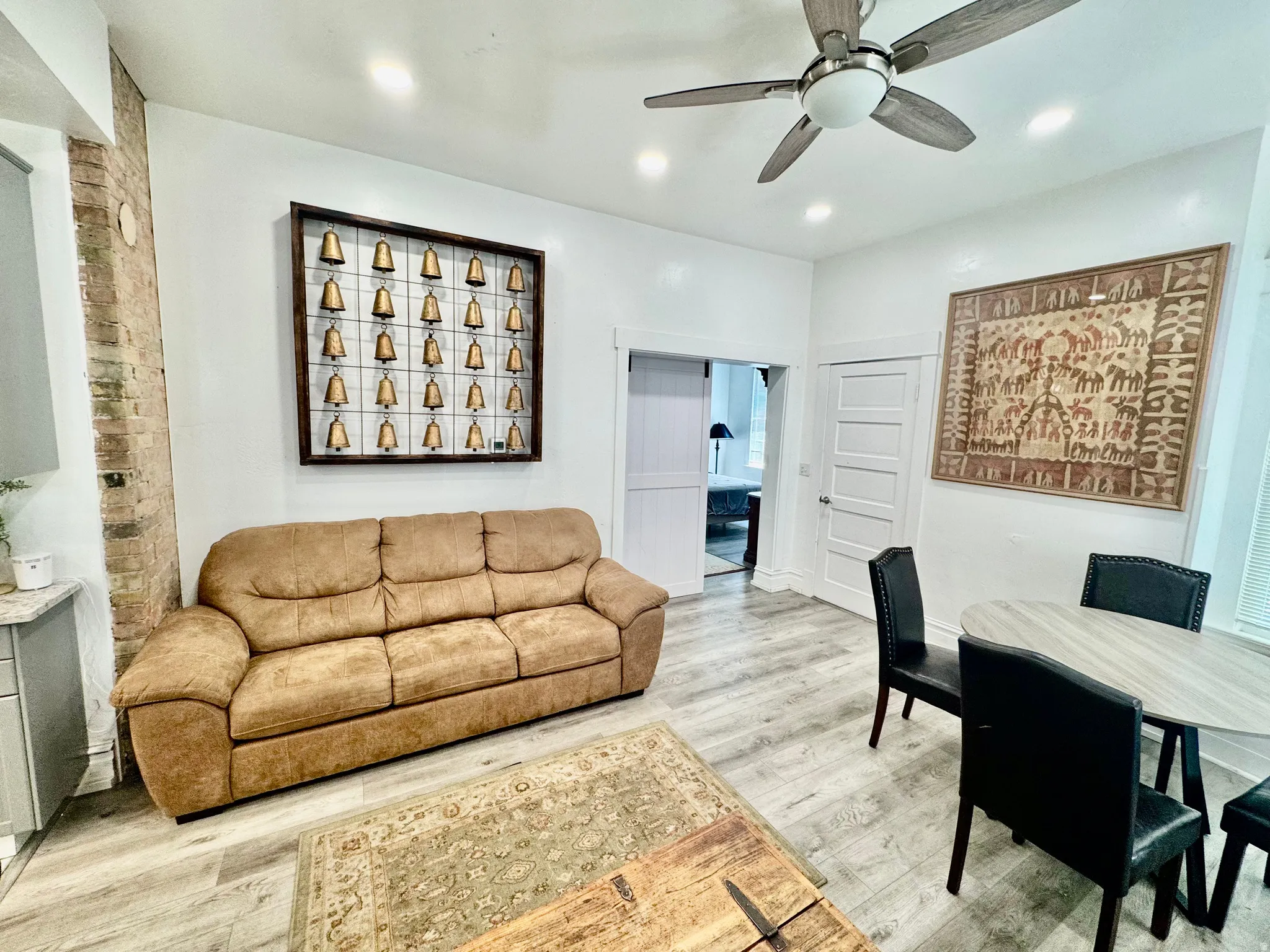 Open-concept living area featuring wood-finish flooring, a contemporary ceiling fan, recessed lighting, and an exposed brick architectural element