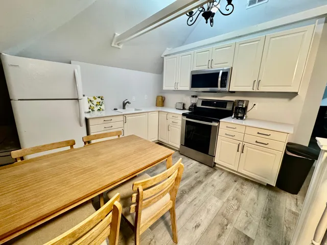 Kitchen area featuring light-toned cabinetry with stainless steel hardware, a white refrigerator, and a stainless steel oven/range with an overhead microwave