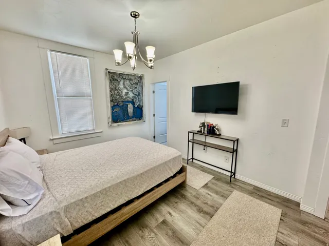 Room featuring wood-finish flooring, a contemporary chandelier, and a window with blinds