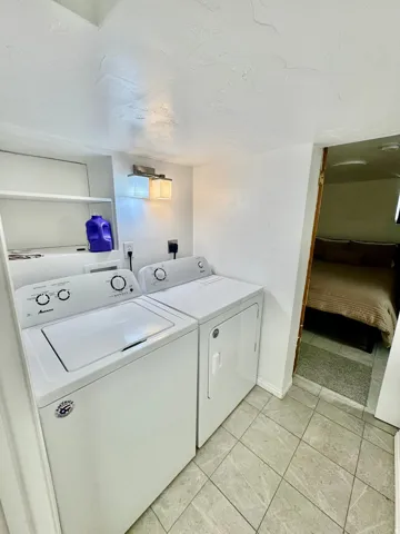 Dedicated laundry area featuring a top-load washing machine and front-load dryer, integrated wall shelving, and overhead lighting