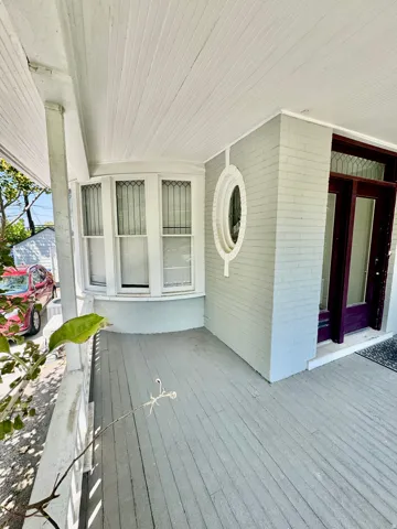 Spacious covered porch with plank flooring, a curved bay window, decorative oval window, and a dark-stained wood entry door with glass panels