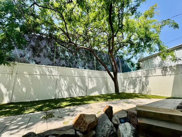 Private backyard featuring a mature tree, manicured lawn, and white privacy fencing