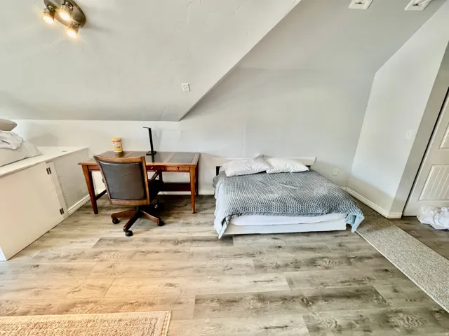 Versatile loft space featuring sloped ceilings, recessed wall panels, and wood-finish flooring