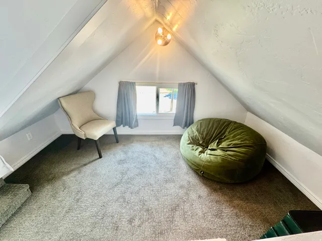 Carpeted attic space featuring sloped ceilings, a window with drapery, and a contemporary ceiling light fixture
