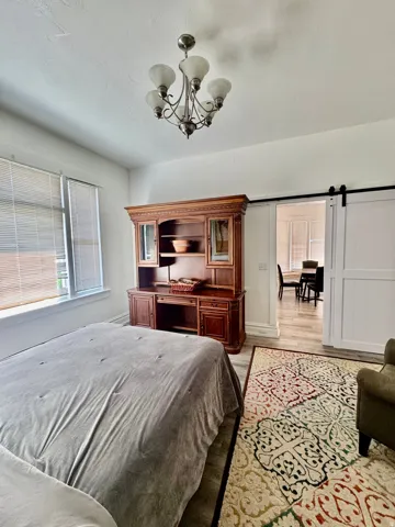 Spacious room featuring light-toned wood-finish flooring, white walls, and a five-light chandelier