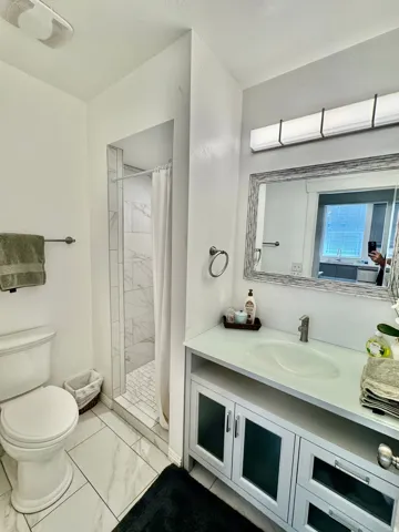 Bathroom featuring a single vanity with an integrated sink, a large framed mirror, and a walk-in shower with tile surround