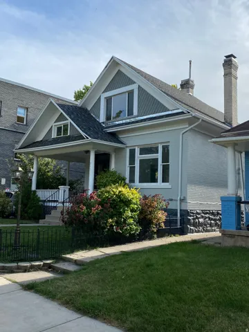 Charming cottage-style home featuring a peaked gable roof with dormer windows, white painted wood siding, and a covered front porch with white columns