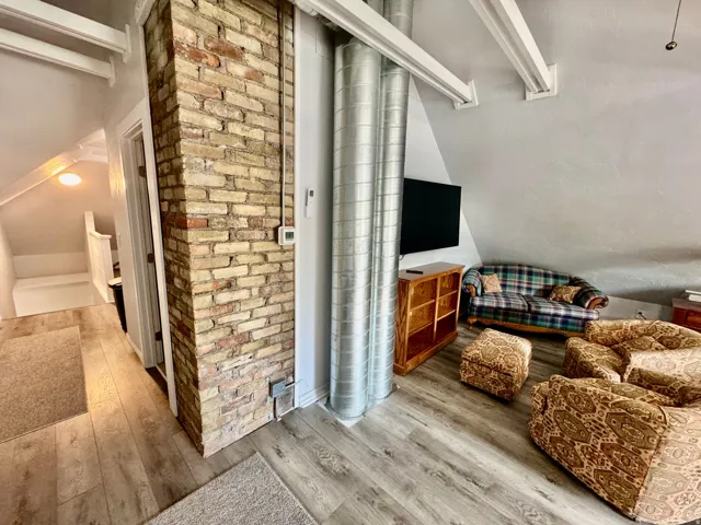 Loft area featuring light wood-finish flooring, exposed brick column, and visible structural beams