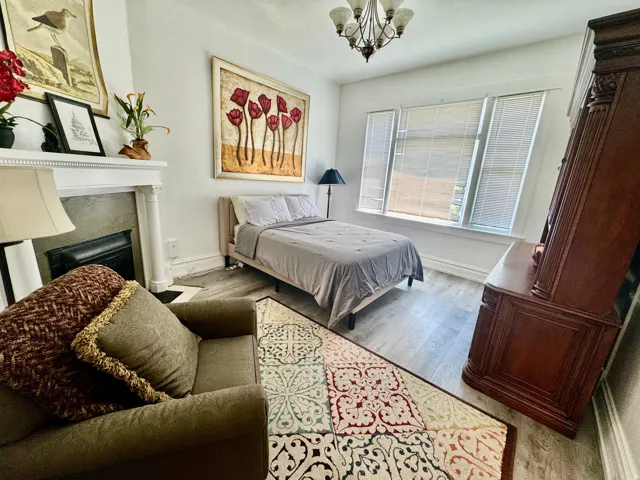 Room featuring light-toned wood-finish flooring, a decorative fireplace with a white mantel, and a multi-pane window with blinds