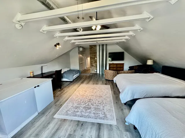 Spacious attic room featuring wood-finish flooring and a sloped ceiling with exposed white beams and ductwork