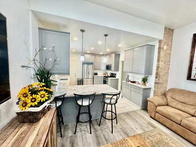 Open-concept kitchen featuring gray shaker-style cabinetry, stainless steel appliances, a spacious island with seating, pendant lighting, and wood-finish flooring
