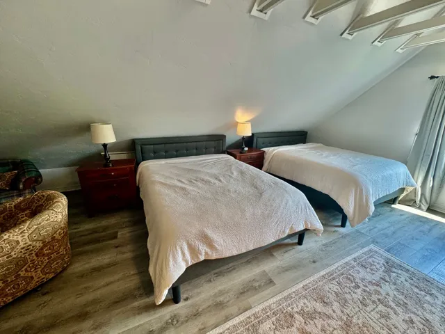 Room featuring sloped ceilings with exposed white rafters, wood-finish flooring, and light-filtering window treatments