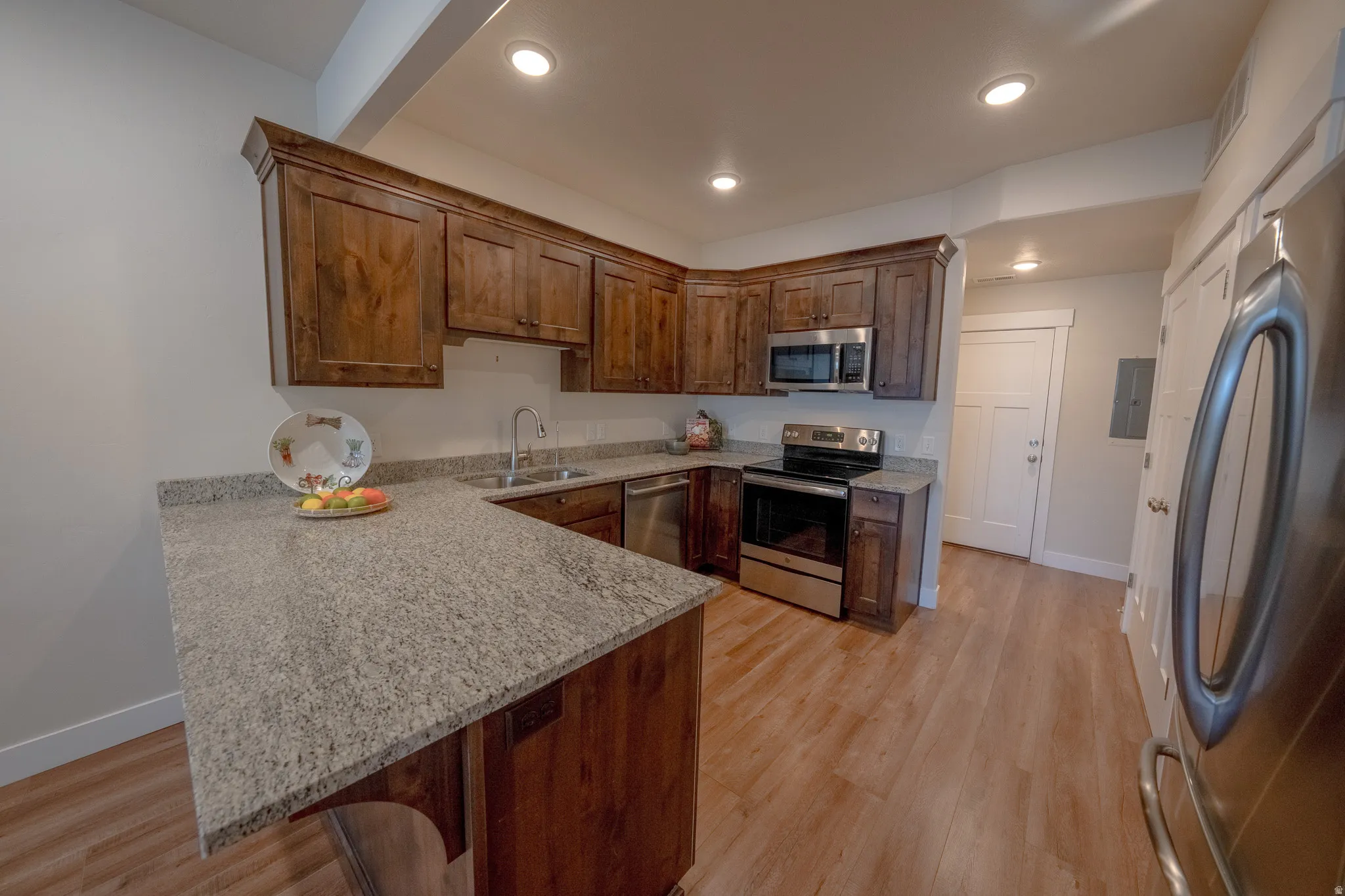 Wood-finish flooring, recessed lighting, wood cabinetry, stainless steel appliances, and a stone countertop