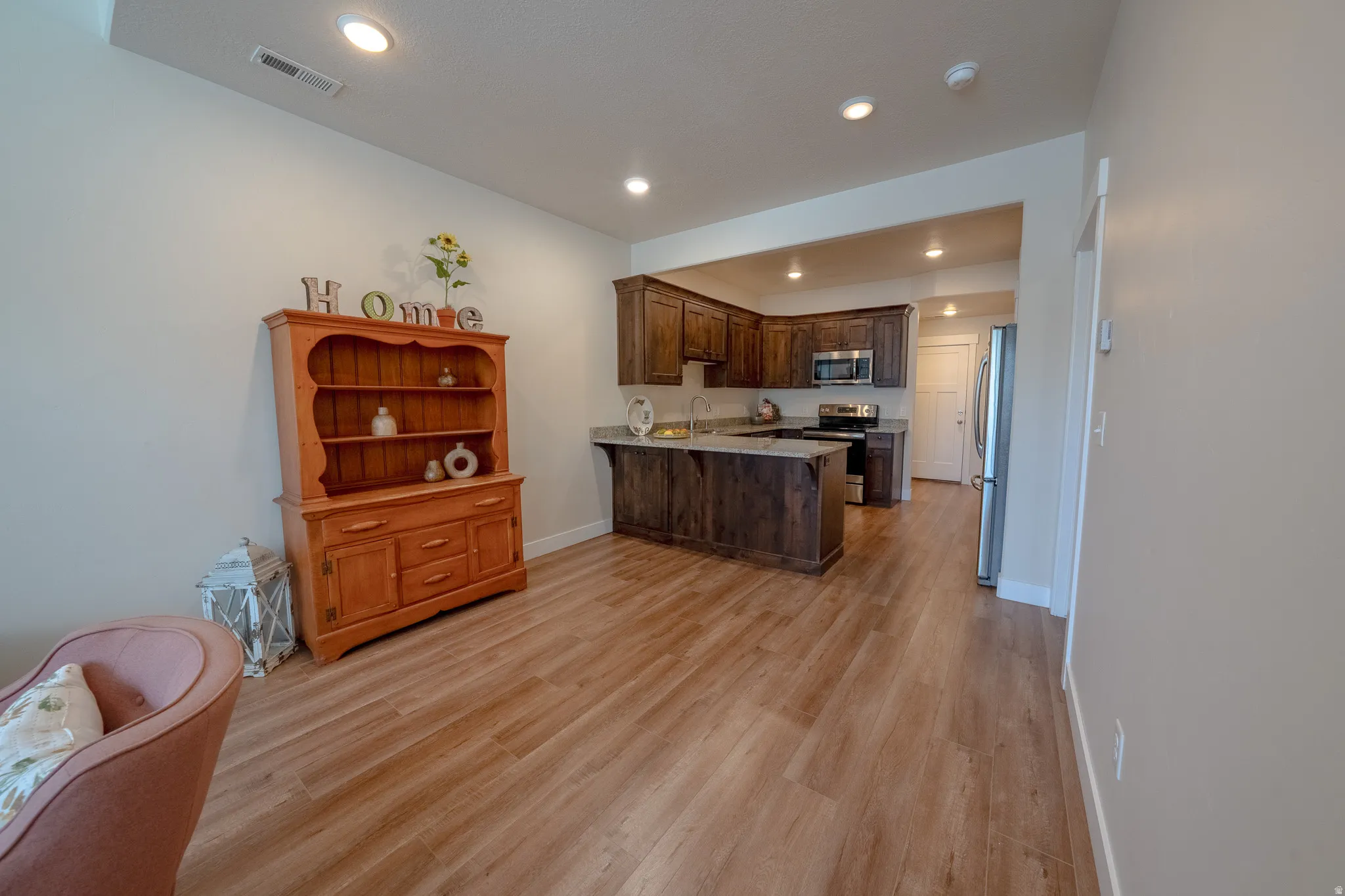 Open-concept living area with wood-finish flooring, recessed lighting, and a kitchen featuring dark wood cabinetry, stainless steel appliances, and a central island