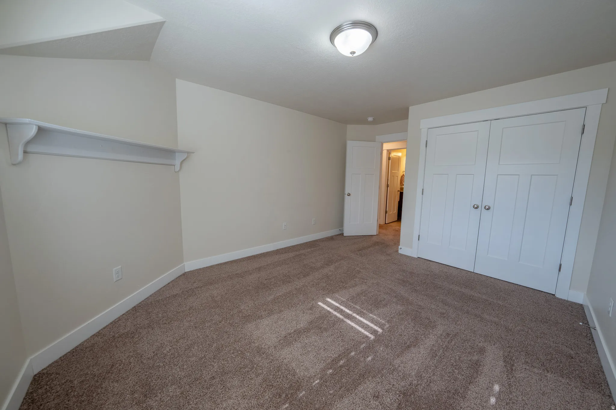 Neutral toned walls, plush carpet flooring, white trim, white shelving, and a semi-flush mount ceiling light