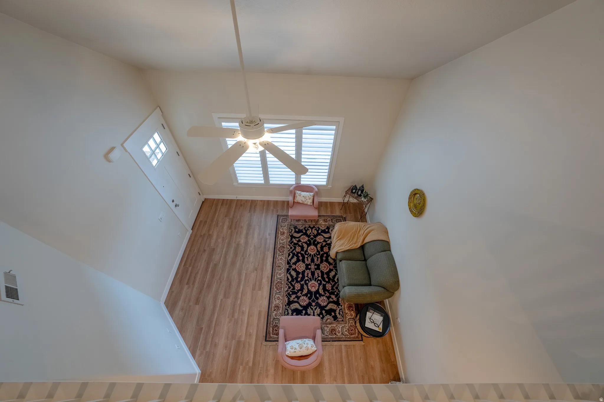 Vaulted ceiling with a ceiling fan, window with horizontal blinds, wood-finish flooring, and white walls
