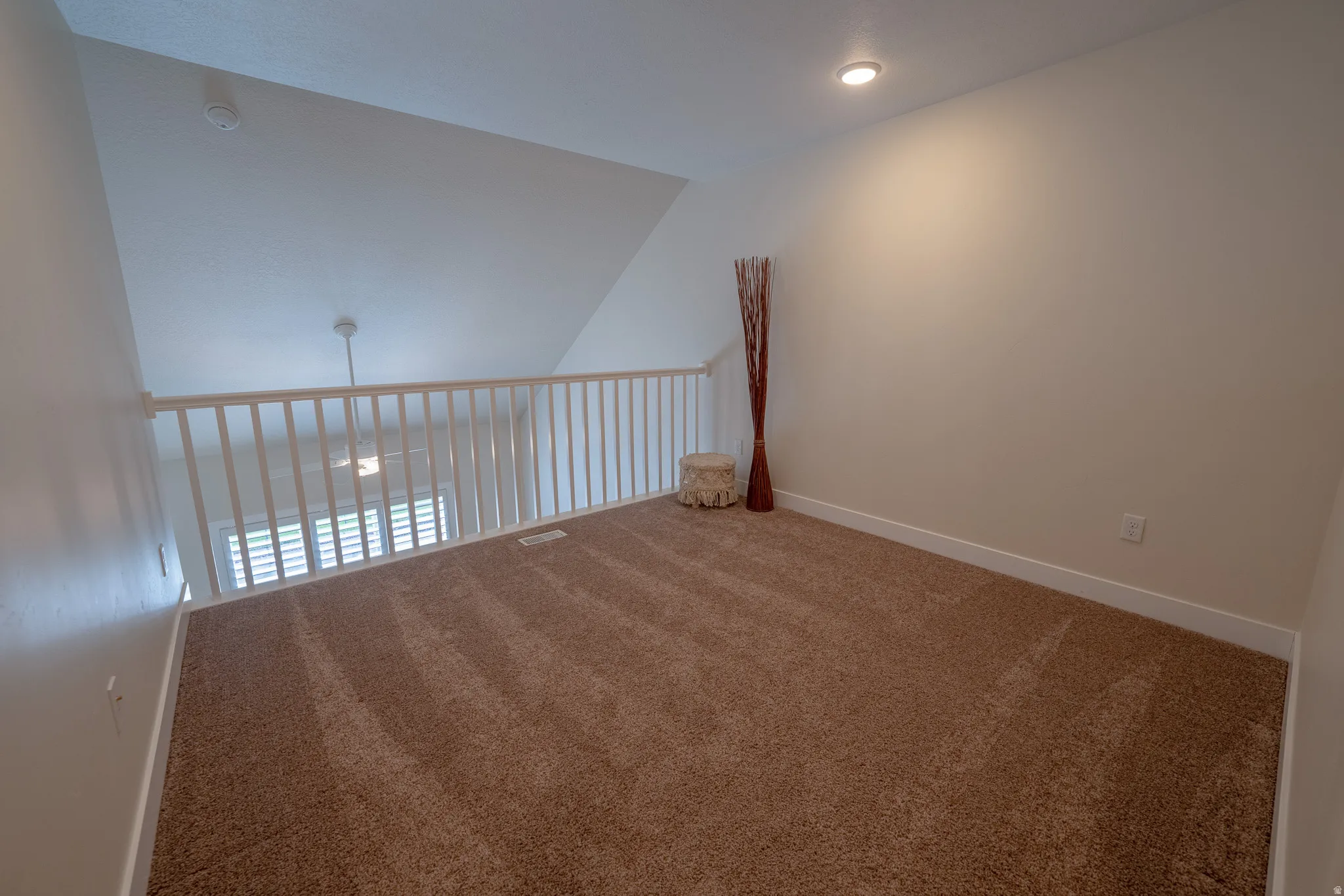 Carpeted loft space featuring an angled ceiling, recessed lighting, white wall railing, and a ceiling fan visible below