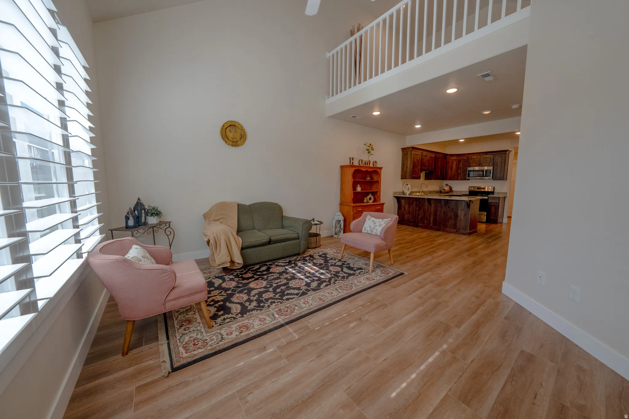 Vaulted ceiling with a ceiling fan, wood-finish flooring, plantation shutters, upper-level railing, and a kitchen featuring dark wood cabinetry